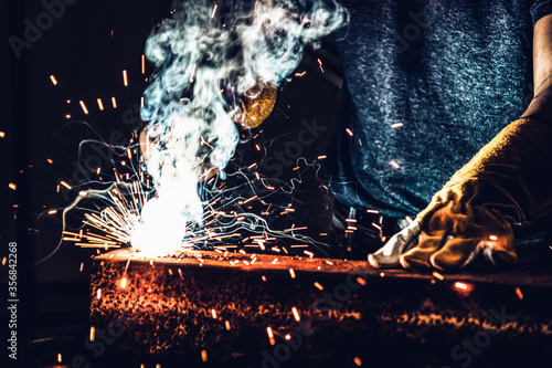 Metal welder working with arc welding machine to weld steel at factory while wearing safety equipment. Metalwork manufacturing and construction maintenance service by manual skill labor concept. photo