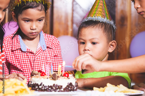 Asian children girls and boys lighting candle on birthday cake together in birthday party