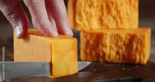 Hands of a man with a knife cut cheddar cheese into pieces.