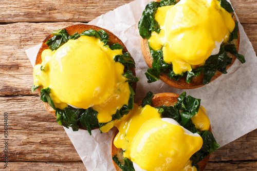 Benedict eggs with spinach and hollandaise sauce on a toasted bun close-up. Horizontal top view
