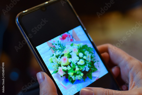 female hand with a phone chooses a bouquet of fresh flowers for home delivery
