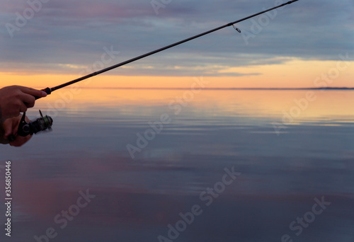 Fishing on the lake at the sunset. Hands of fisherman with fishing rod. Macro shot. Fishing rod and hands of fisherman over lake water. Spinning rod. Fishing tackle
