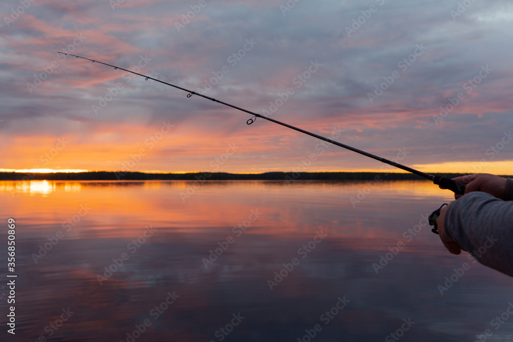 Fishing on the lake at the sunset. Hands of fisherman with fishing rod. Macro shot. Fishing rod and hands of fisherman over lake water. Spinning rod. Fishing tackle