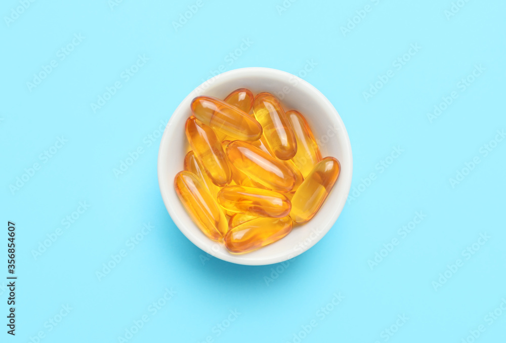 Bowl with fish oil capsules on color background Bowl with fish oil capsules on color background