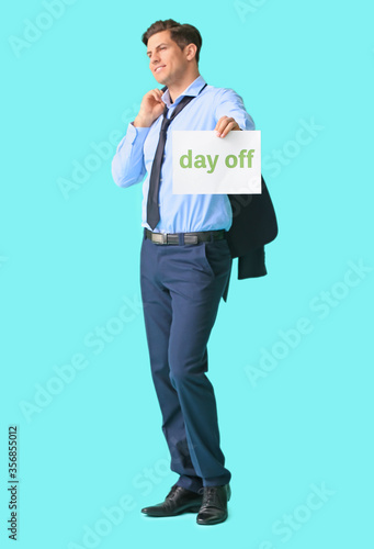 Young businessman holding paper with text DAY OFF against color background © Pixel-Shot