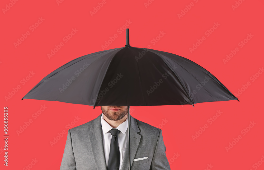 Handsome businessman with umbrella on color background