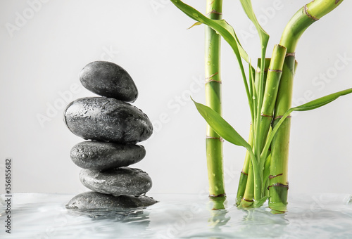 Stack of spa stones and bamboo in water against light background