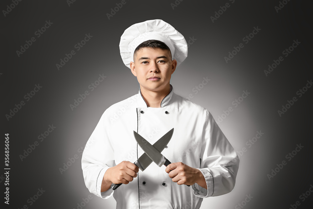 Handsome Asian chef with knives on dark background Handsome Asian chef with knives on dark background