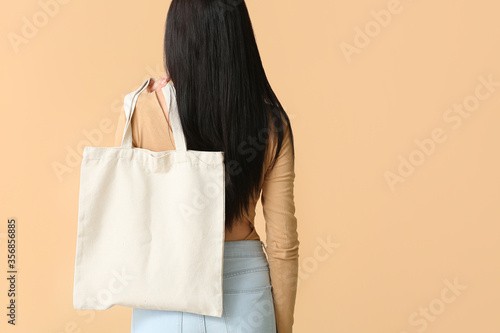 Young woman with eco bag on color background, back view