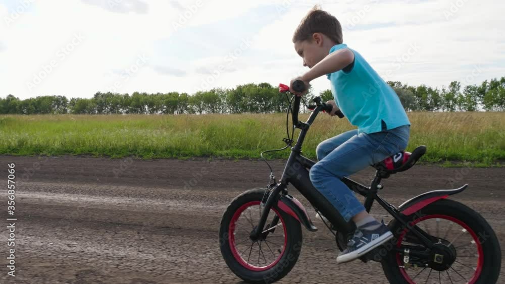 A boy rides a bike on a country road on a Sunny day. A happy child rides a Bicycle, gaining speed. Active rest in the open air, the achievement of the goal. A boy rides a bike on a country road on a Sunny day. A happy child rides a Bicycle, gaining speed. Active rest in the open air, the achievement of the goal.