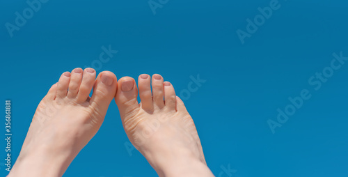 feet with beige pedicure on a turquoise background. The image on the left side of the frame.