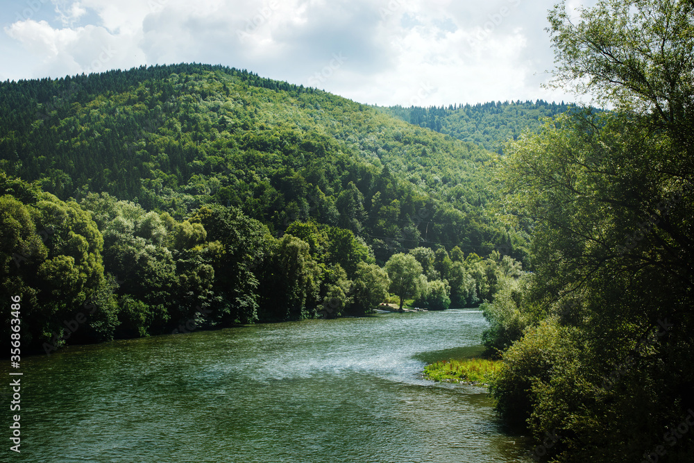 Summer landscape with mountain river running among hills covered with green woodland Summer landscape with mountain river running among hills covered with green woodland