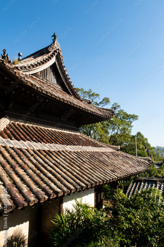 Wooden carved, decorated roofs of buddhist temple in Nagasaki, Japan among green trees. 