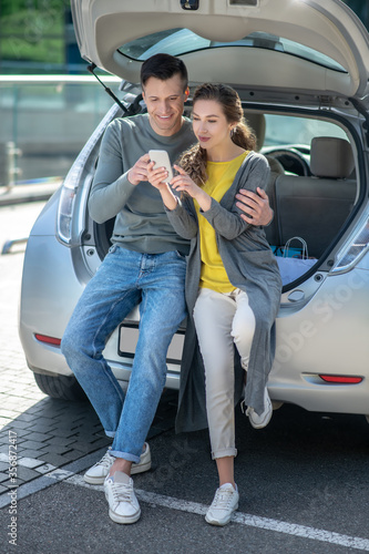 Young man and woman with smartphone are resting near the car © zinkevych