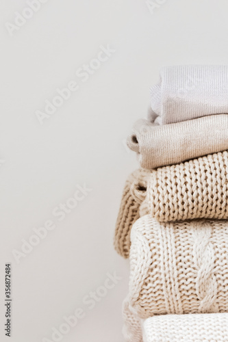 Close up stack of neatly folded warm knitted woolen sweaters on a beige background. Capsule wardrobe, wardrobe, minimalism, knitted texture, order, comfort, macro. Vertical with copy space for text. © Smart Blonde 