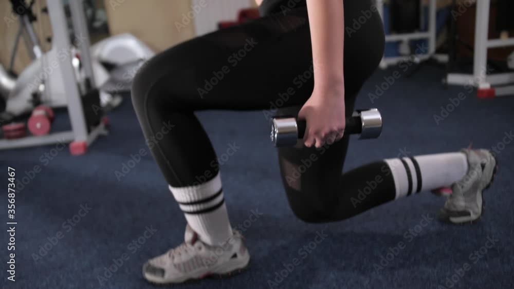 Fitness girl in a sport suit makes a squat from the rack of the lunge with dumbbells in her hands. Fitness girl in a sport suit makes a squat from the rack of the lunge with dumbbells in her hands.
