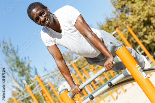 Active african  american man doing workout at pull-up bar  in park © JackF