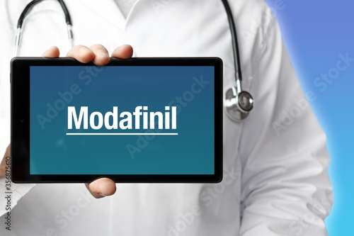 Modafinil. Arzt mit Stethoskop hält Tablet-Computer in Hand. Text im Display. Blauer Hintergrund. Krankheit, Gesundheit, Medizin photo