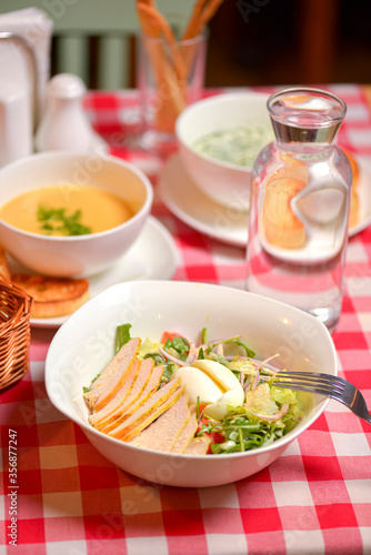 Chicken Caesar salad served in a white bowl. Traditional salad with chicken meat, eggs, tomatoes. Dinner in restaurant.