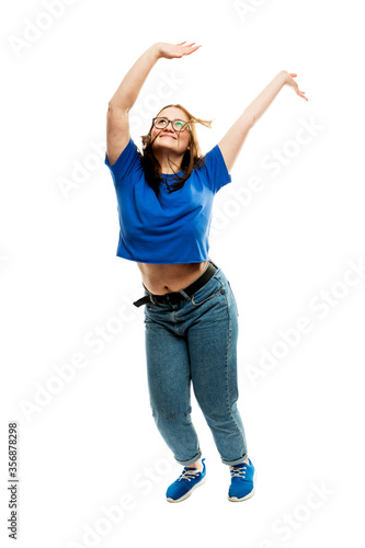 Laughing fat young girl in glasses and jeans emotionally jumps up. Energy and movement. Isolated on a white background. Vertical.