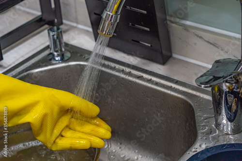 Human wearing plastic gloves and rinsing water at the sink