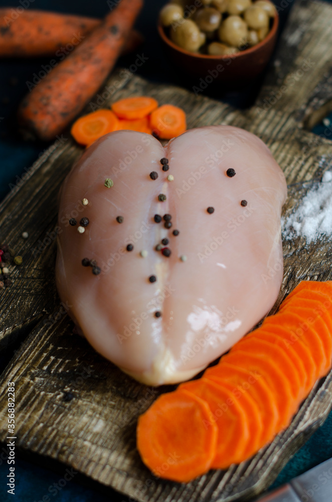 fresh chicken breast on a wooden board with raw carrots and spices