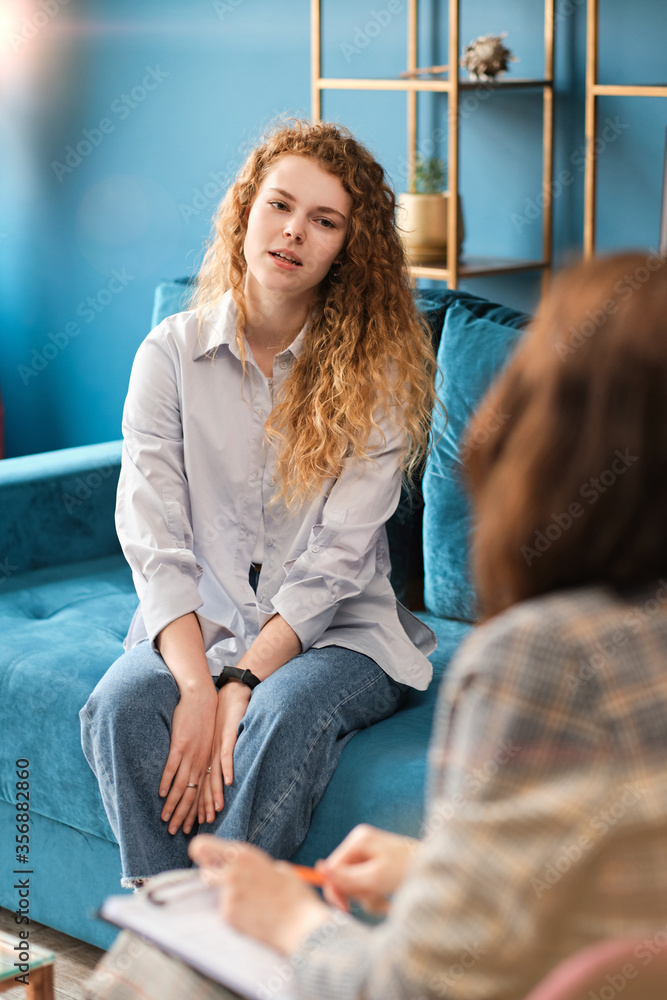 Unhappy red-haired woman talking to a female psychologist. Discusses her problems, mental trauma. Consultation in the office on the sofa. Unhappy red-haired woman talking to a female psychologist. Discusses her problems, mental trauma. Consultation in the office on the sofa.