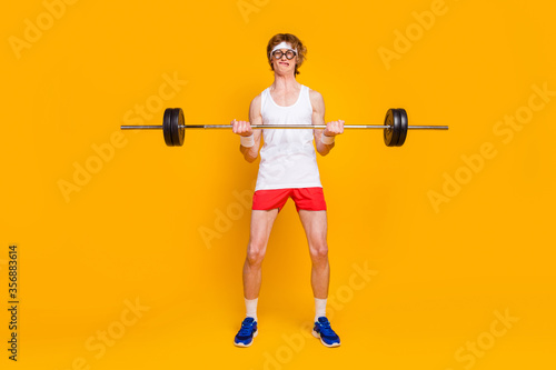 Full length body size view of his he nice attractive weak slim sportive guy lifting heavy barbell individual work out isolated over bright vivid shine vibrant yellow color background photo