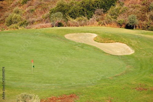Elevated view across a golfing green, bunker and flag near Marbella, Spain.