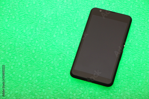 Black smartphone lies on a bright green background. The background is highlighted below. photo