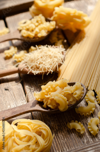 different types of raw pasta on a wooden background in wooden spoons