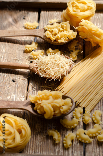 different types of raw pasta on a wooden background in  wooden spoons