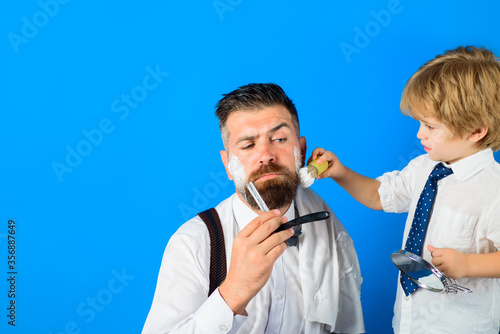Shaving beard in barbershop. Beard care. Little barber. Barbershop concept. Salon for men. Son and dad in barber shop. Assistant for dad. Fathers day.