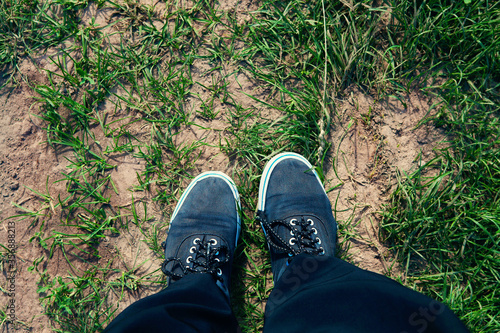 Legs in old worn sneakers on road with grass, top view. © Liudmyla