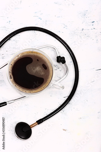 Cup of coffee and stethoscope on white table.