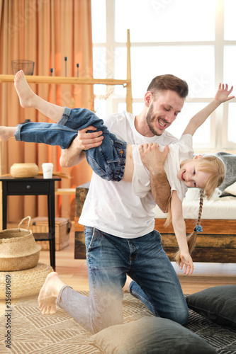 Father and daughter. Handsome young man and little cute girl play on the carpet at home, hug, have fun. Dad and child laugh. Father's day.