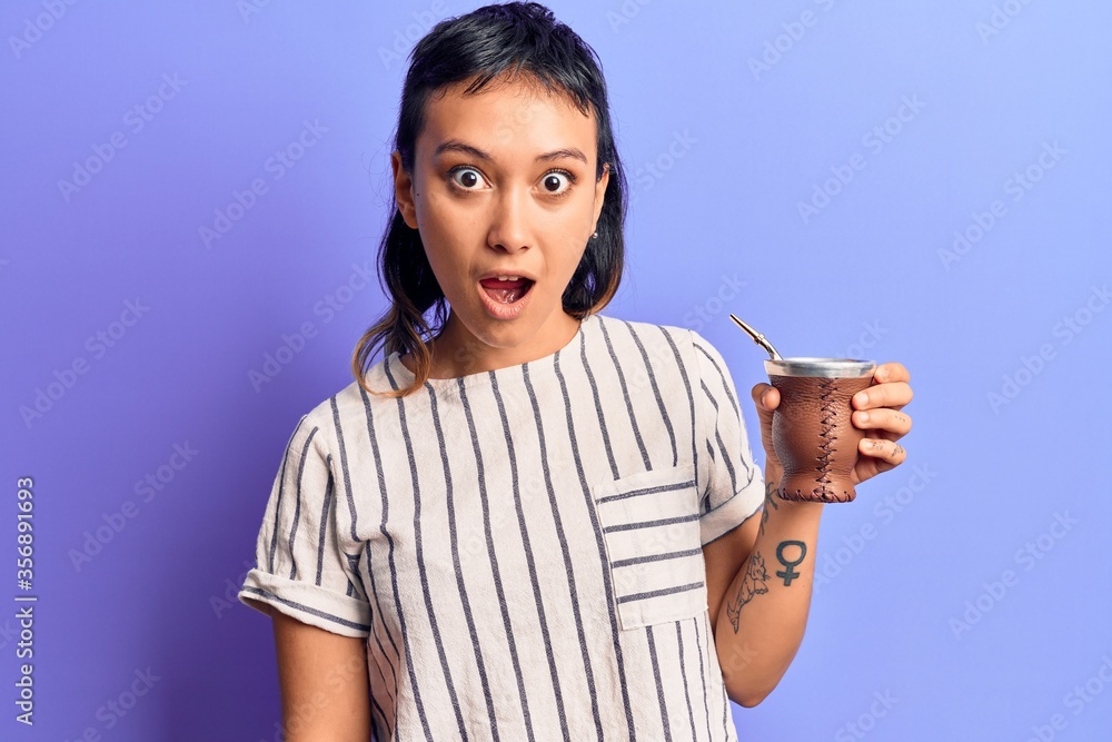 Young woman drinking mate infusion scared and amazed with open mouth for surprise, disbelief face Young woman drinking mate infusion scared and amazed with open mouth for surprise, disbelief face