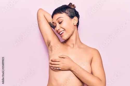 Young beautiful woman shirtless smiling happy. Standing with smile on face showing hairy armpit over isolated pink background photo
