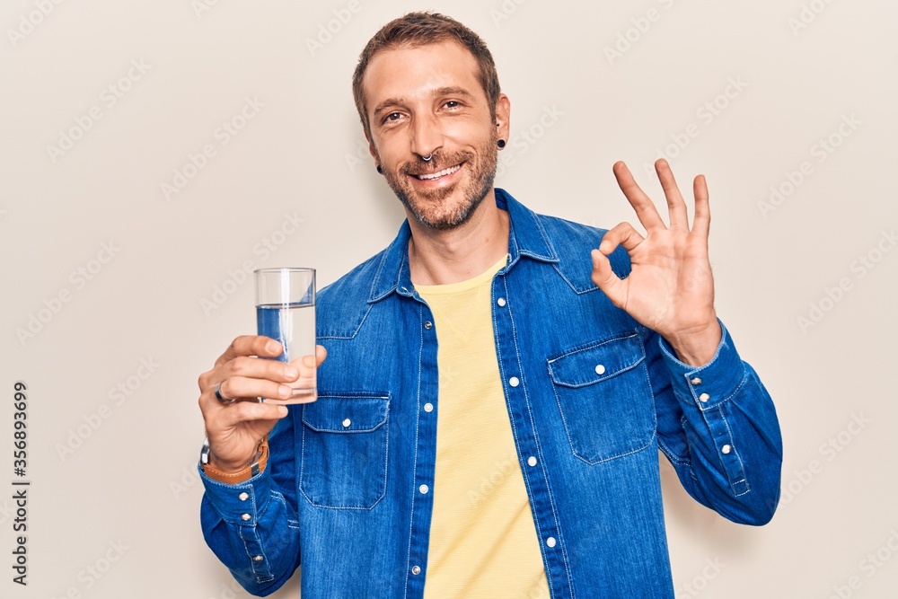 Young handsome man drinking glass of water doing ok sign with fingers, smiling friendly gesturing excellent symbol Young handsome man drinking glass of water doing ok sign with fingers, smiling friendly gesturing excellent symbol
