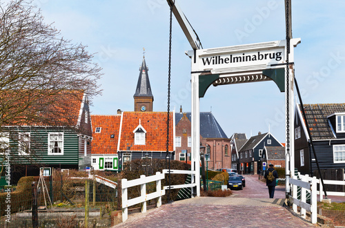 Netherlands, North Holland, Marken island. View of a typical Dutch white drawbridge, characteristic green wooden houses on the Kerkbuurt street and  and a Protestant church photo