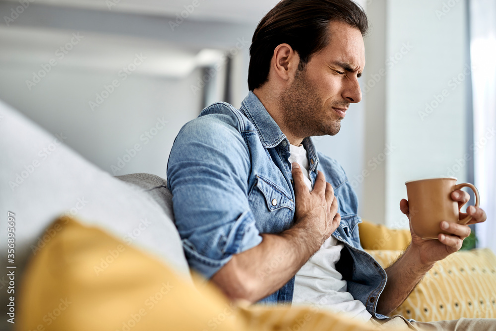 Fotografie Young man having a chest pain while drinking tea at home.