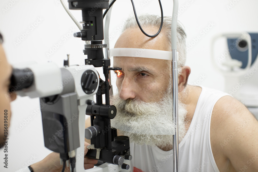 Doctor Optometrist examining bearded senior man eyes with special eye equipment. Doctor Optometrist examining bearded senior man eyes with special eye equipment.
