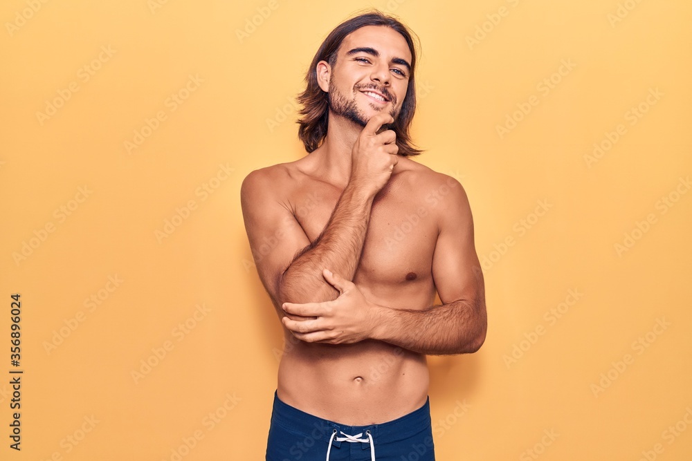 Fototapeta premium Young handsome man wearing swimwear shirtless smiling looking confident at the camera with crossed arms and hand on chin. thinking positive.