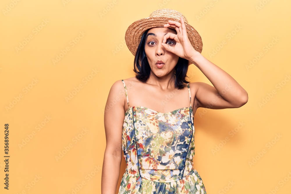 Young beautiful latin woman wearing summer hat doing ok gesture shocked with surprised face, eye looking through fingers. unbelieving expression. Young beautiful latin woman wearing summer hat doing ok gesture shocked with surprised face, eye looking through fingers. unbelieving expression.