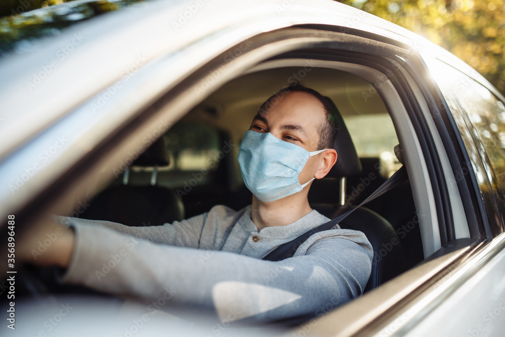 A man drives a car wearing medical mask during coronavirus outbreak. Taxi driver delivers his passanger to the destination. Social distance, new normal, virus spread prevention and treat concept. A man drives a car wearing medical mask during coronavirus outbreak. Taxi driver delivers his passanger to the destination. Social distance, new normal, virus spread prevention and treat concept.