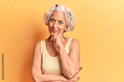 Senior grey-haired woman wearing casual clothes looking confident at the camera smiling with crossed arms and hand raised on chin. thinking positive. photo