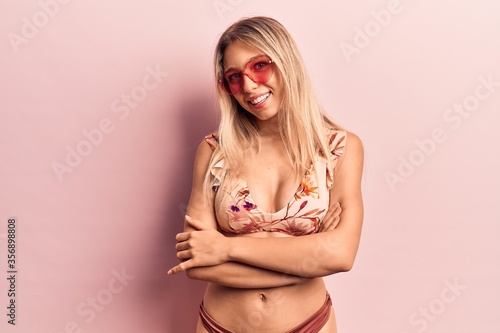 Young beautiful blonde woman wearing bikini heart sunglasses happy face smiling with crossed arms looking at the camera. positive person. © Krakenimages.com