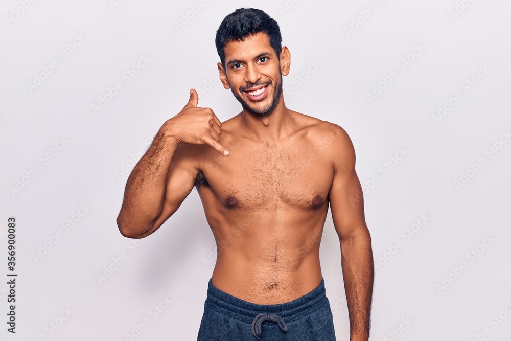 Young latin man standing shirtless smiling doing phone gesture with hand and fingers like talking on the telephone. communicating concepts. Young latin man standing shirtless smiling doing phone gesture with hand and fingers like talking on the telephone. communicating concepts.