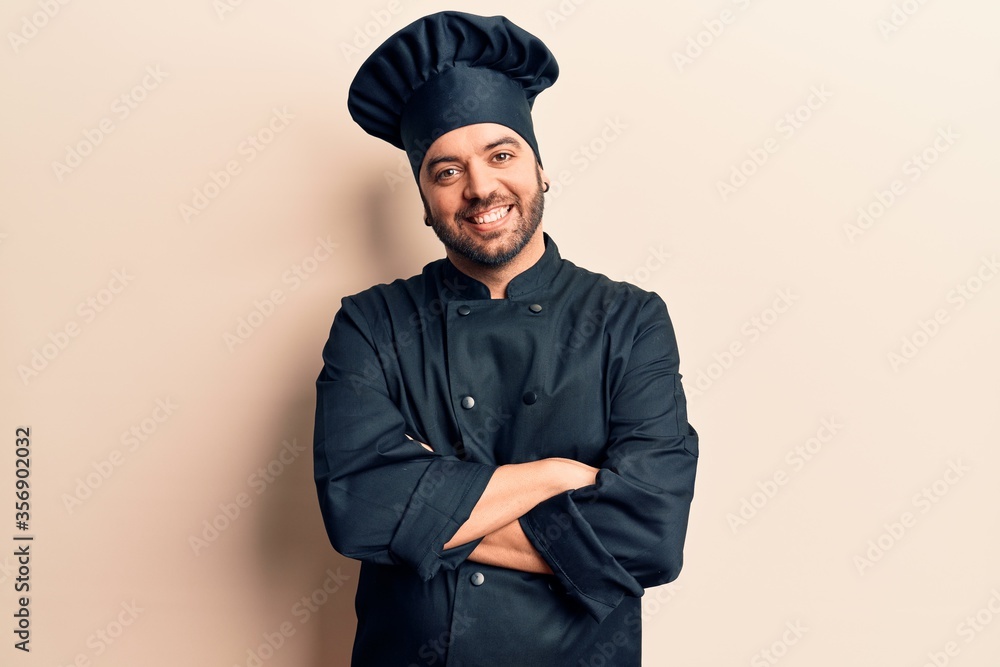 Young hispanic man wearing cooker uniform happy face smiling with crossed arms looking at the camera. positive person. Young hispanic man wearing cooker uniform happy face smiling with crossed arms looking at the camera. positive person.