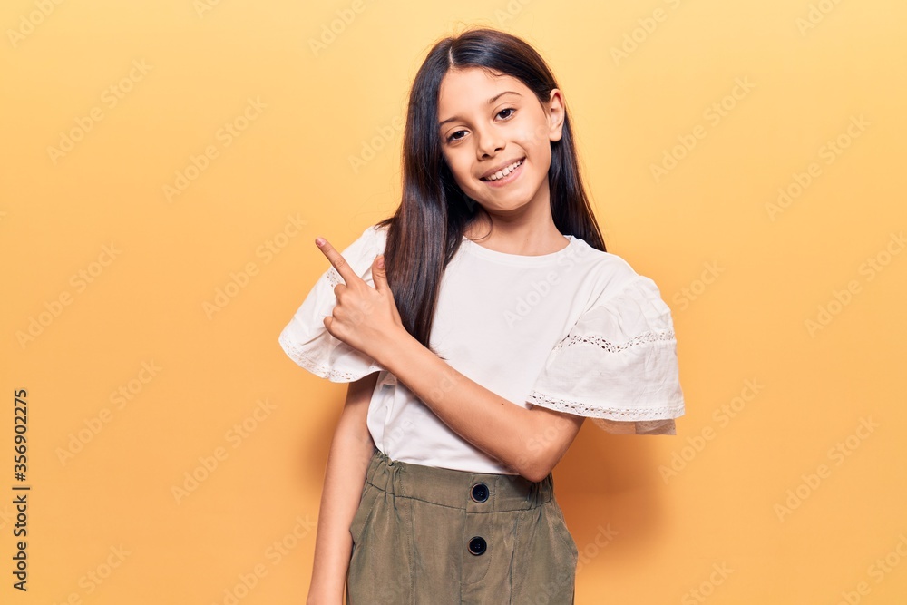 Beautiful child girl wearing casual clothes smiling cheerful pointing with hand and finger up to the side Beautiful child girl wearing casual clothes smiling cheerful pointing with hand and finger up to the side